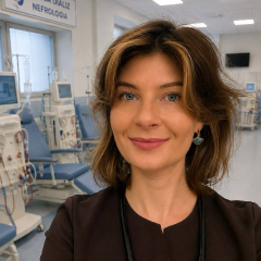 Zdjęcie lek. Joanna Ziółkowska-Kuszewska. Lekarka w ciemnym fartuchu ze stetoskopem na szyi w sali stacji dializ i nefrologii, w tle widać stanowiska do dializ oraz aparaturę medyczną.
